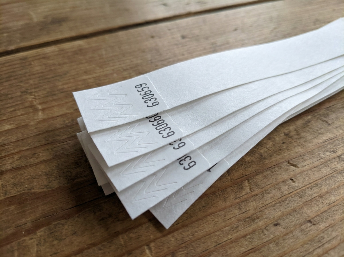 Nærbillede af Tyvek-armbånd med sekventiel sorttrykt nummerering anbragt i vifte på et adgangskontrolbord ved en begivenhed