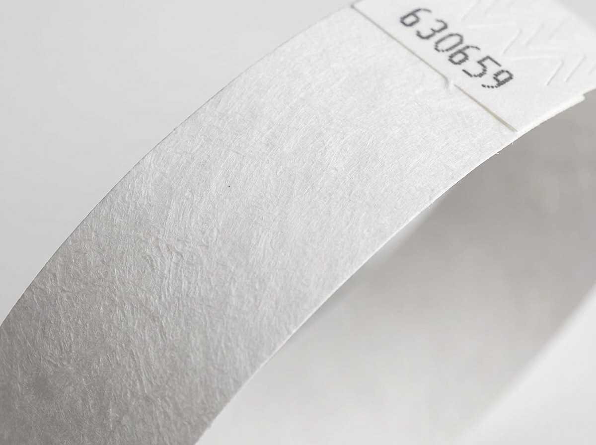 Naerbillede af overfladen pa et hvidt Tyvek-armbånd af ikke-vaevet materiale, der viser den karakteristiske tekstur af hojttathedspolyethylen